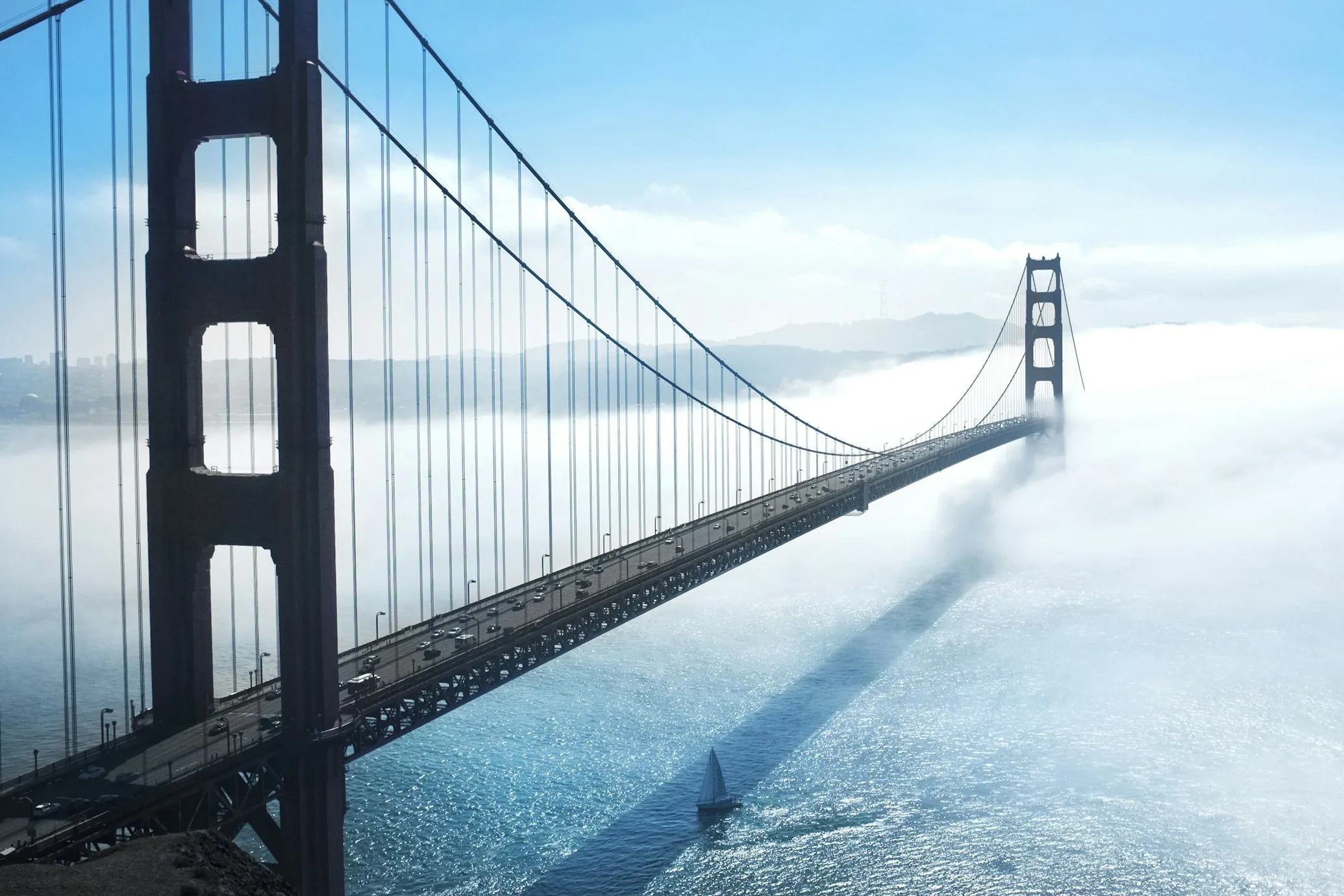 Suspension bridge over body of water with dense fog and hills in background.